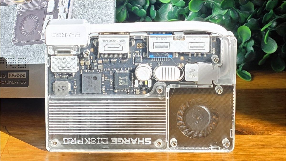 Sharge’s Disk Pro SSD on a wooden shelf, showing its clearly labeled USB and video ports, as well as its transparent cover.